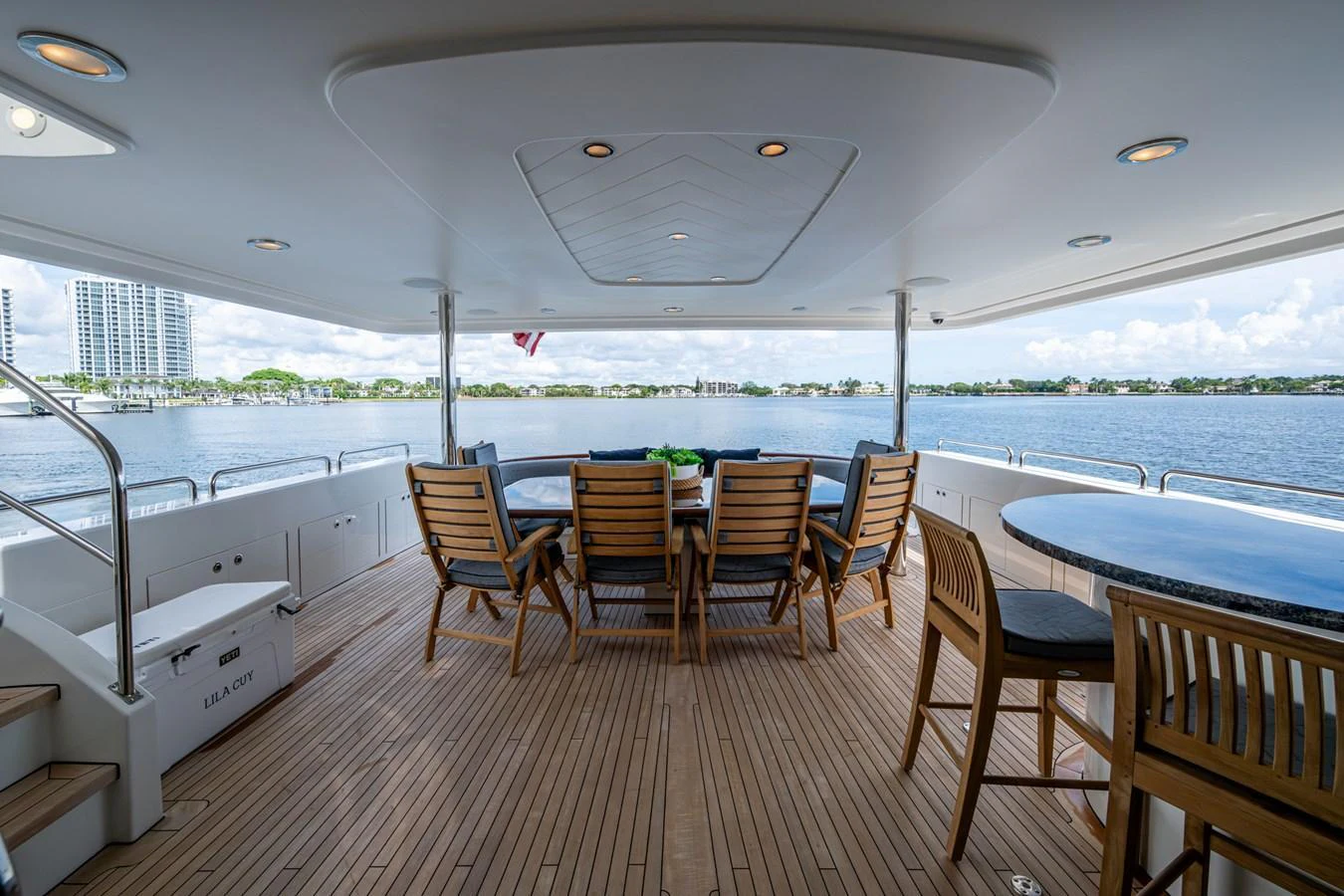 The aft deck features a spacious dining area with wooden chairs and tables, offering a serene view of the water. aboard LILA CUY Yacht for Sale
