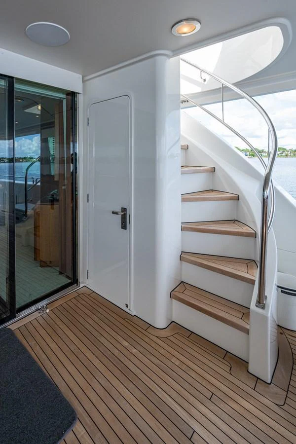 A sleek staircase with wooden steps leads to the upper deck, complemented by a modern door and glass sliding door. aboard LILA CUY Yacht for Sale
