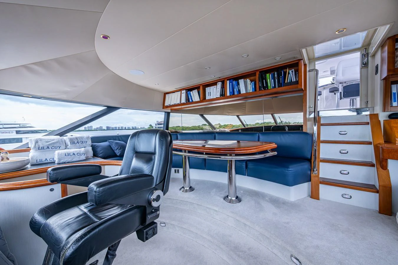 The salon features a comfortable seating area with a table and a well-organized bookshelf, creating a cozy and functional space. aboard LILA CUY Yacht for Sale