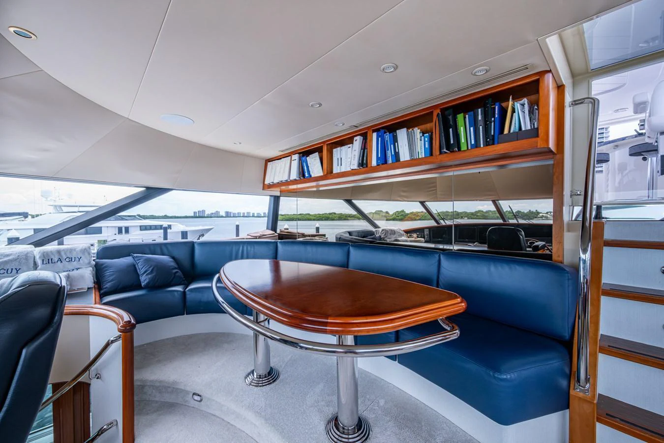 The yacht's salon features a curved seating area with a polished wooden table and built-in shelving. aboard LILA CUY Yacht for Sale