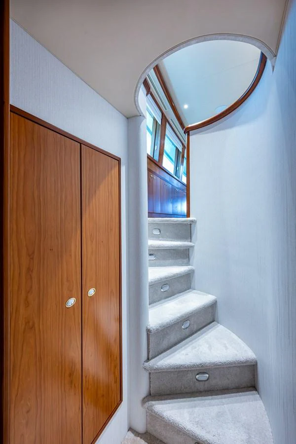 A stylish interior staircase with wooden accents and plush carpeting leads to the upper deck. aboard LILA CUY Yacht for Sale