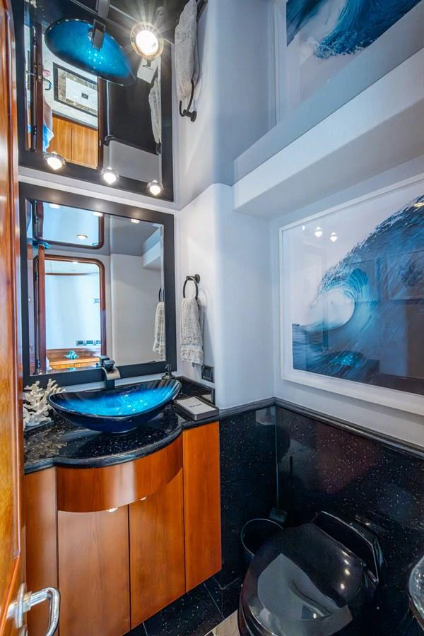 The yacht's bathroom features a modern design with a striking blue glass sink and elegant wood cabinetry. aboard LILA CUY Yacht for Sale