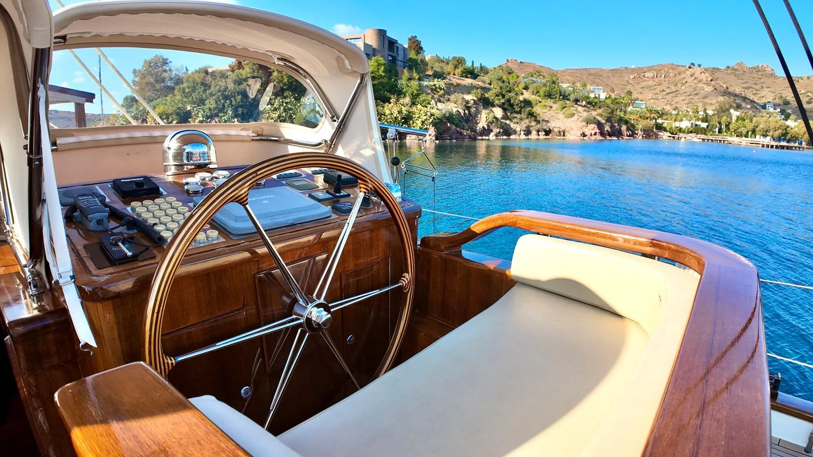 The helm station offers a classic wooden steering wheel with a comfortable seating area, overlooking serene waters. aboard PORTOBELLO Yacht for Sale