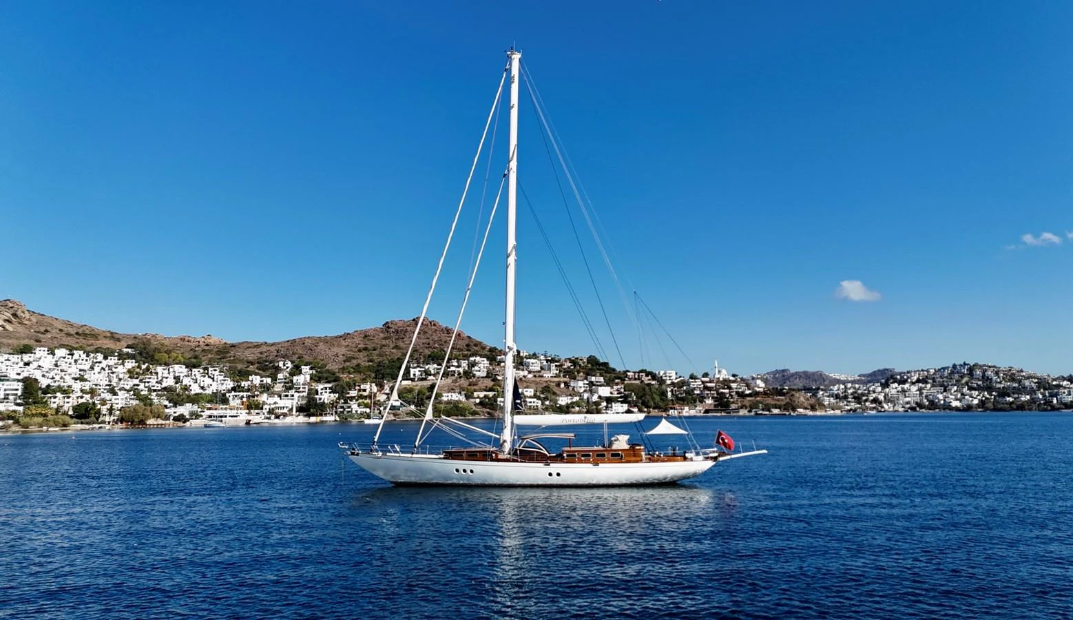 A sleek sailing yacht glides gracefully on calm waters with a picturesque coastal backdrop. aboard PORTOBELLO Yacht for Sale