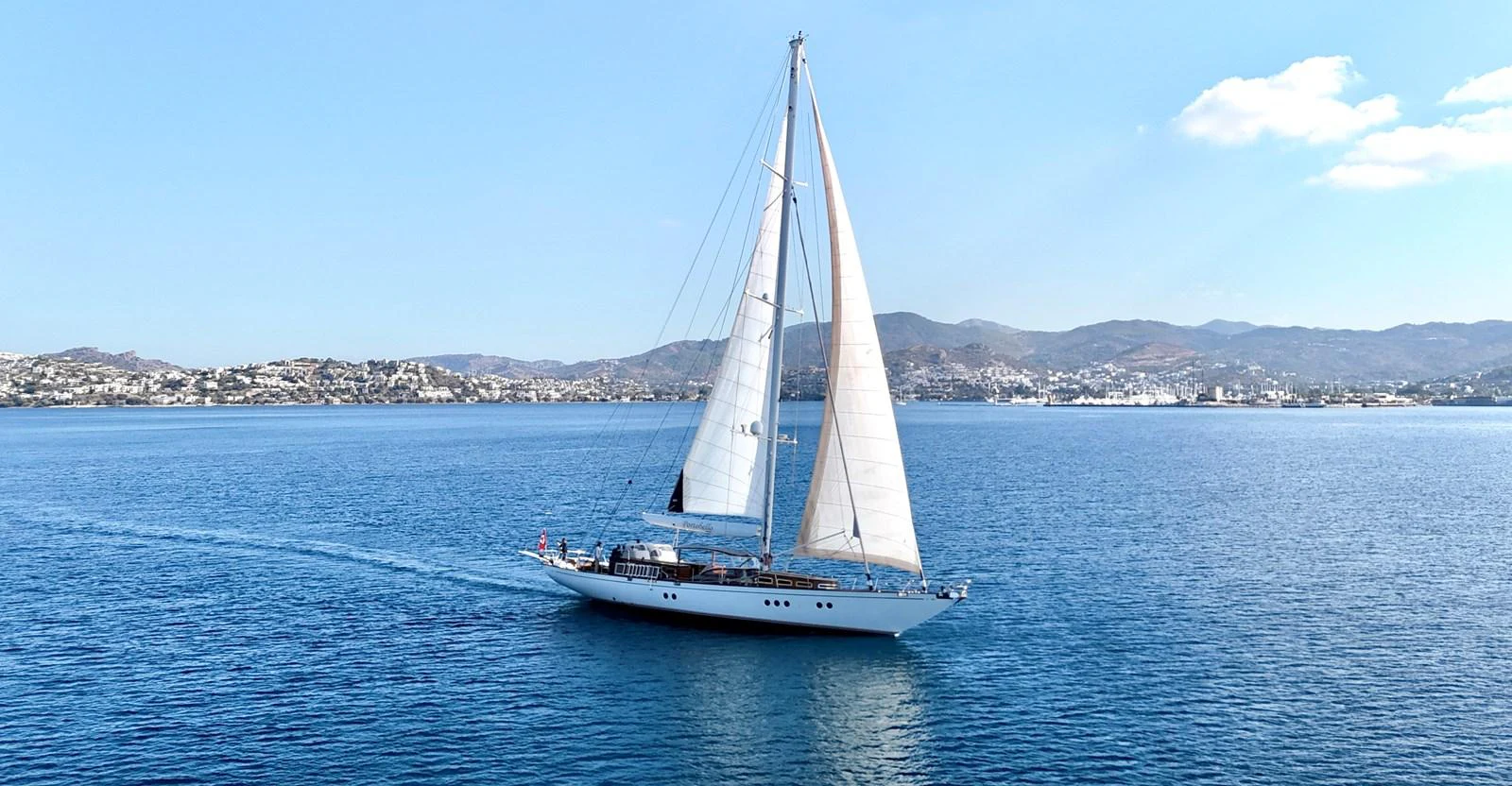 A stunning sailing yacht glides gracefully across calm waters with picturesque coastal scenery in the background. aboard PORTOBELLO Yacht for Sale