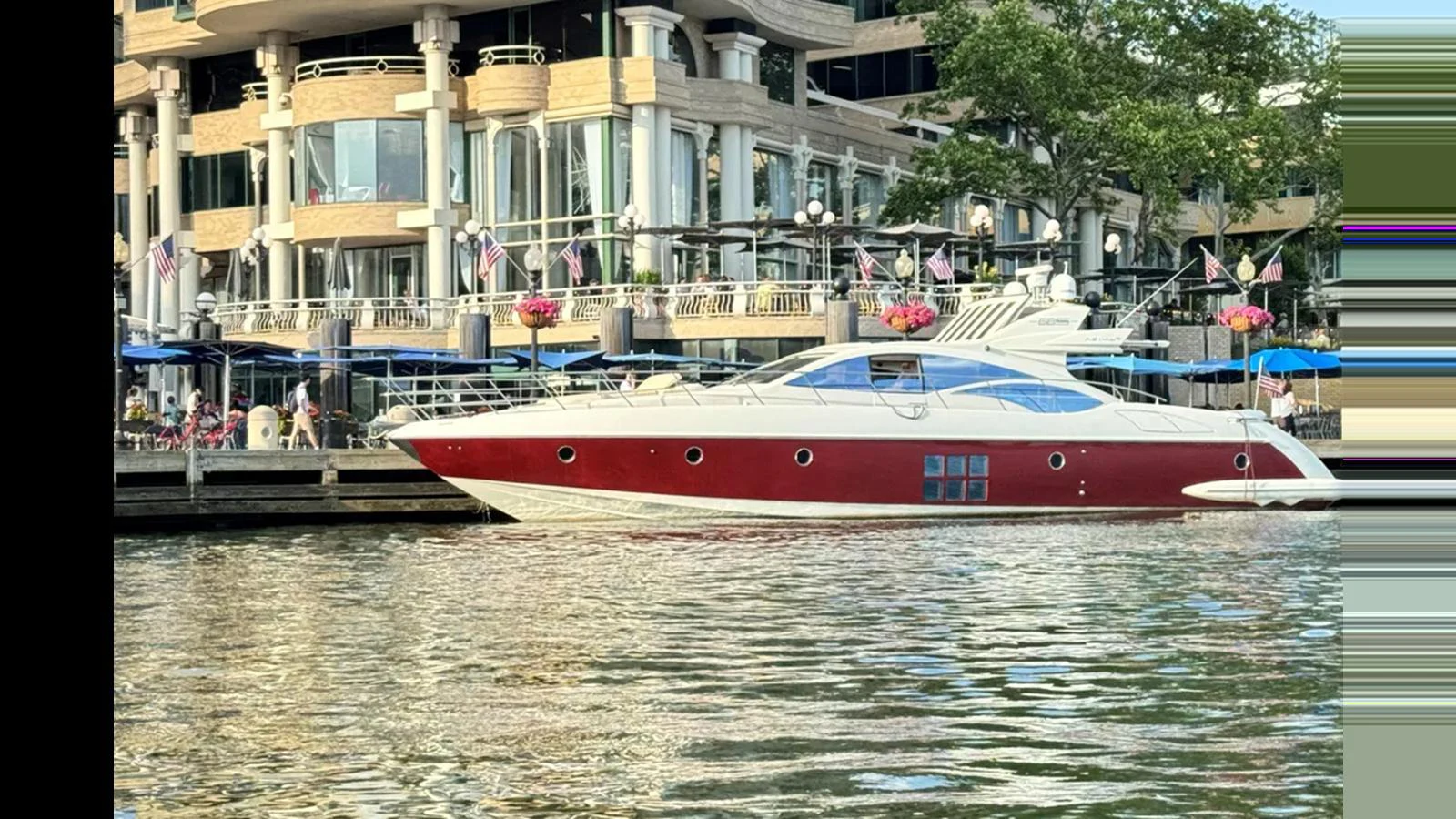 A sleek yacht with a striking red hull is docked beside a luxurious waterfront building. aboard 2007 AZIMUT 68S Yacht for Sale