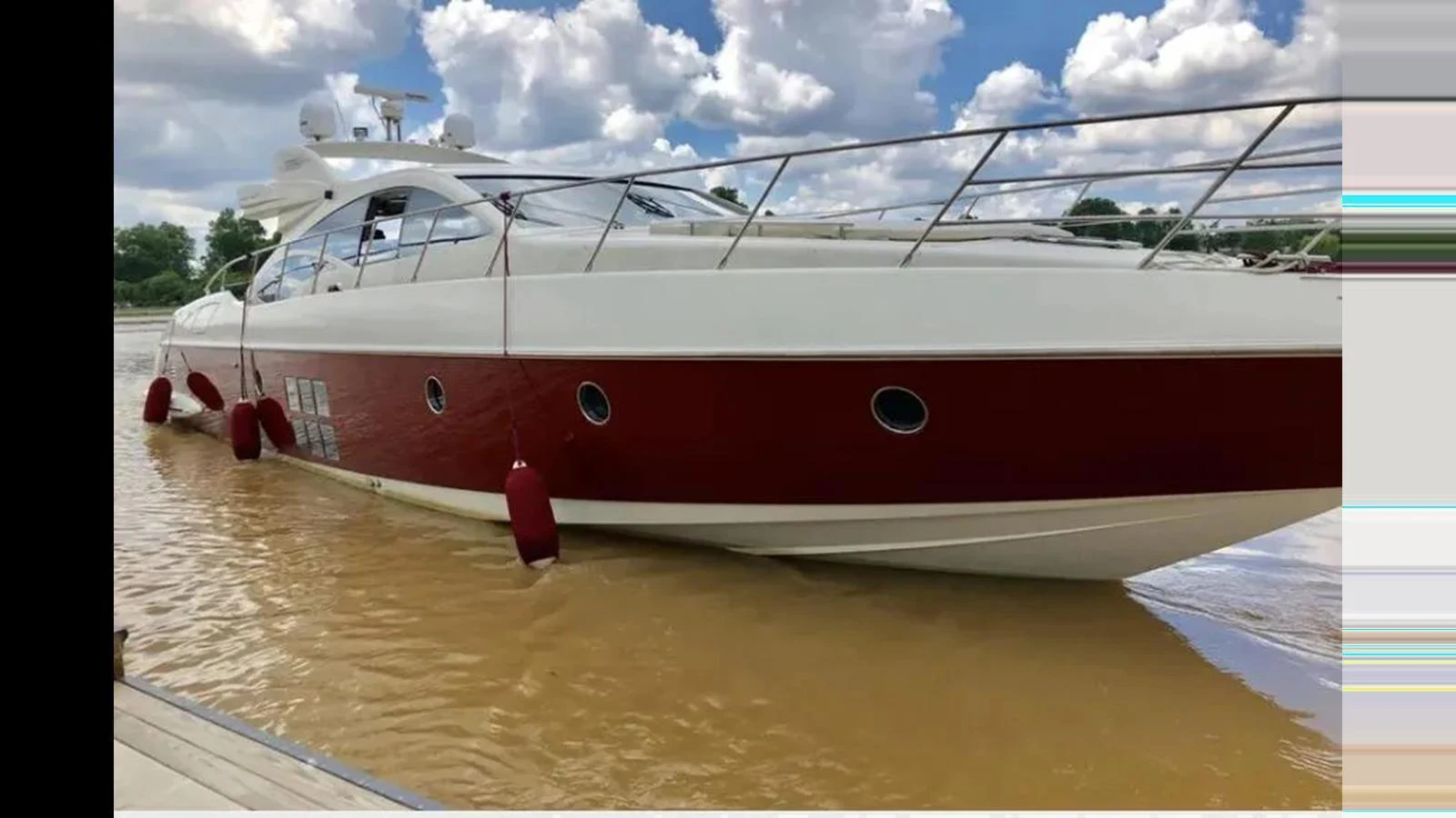 A sleek and modern yacht with a striking red and white exterior is docked in calm waters under a partly cloudy sky. aboard 2007 AZIMUT 68S Yacht for Sale