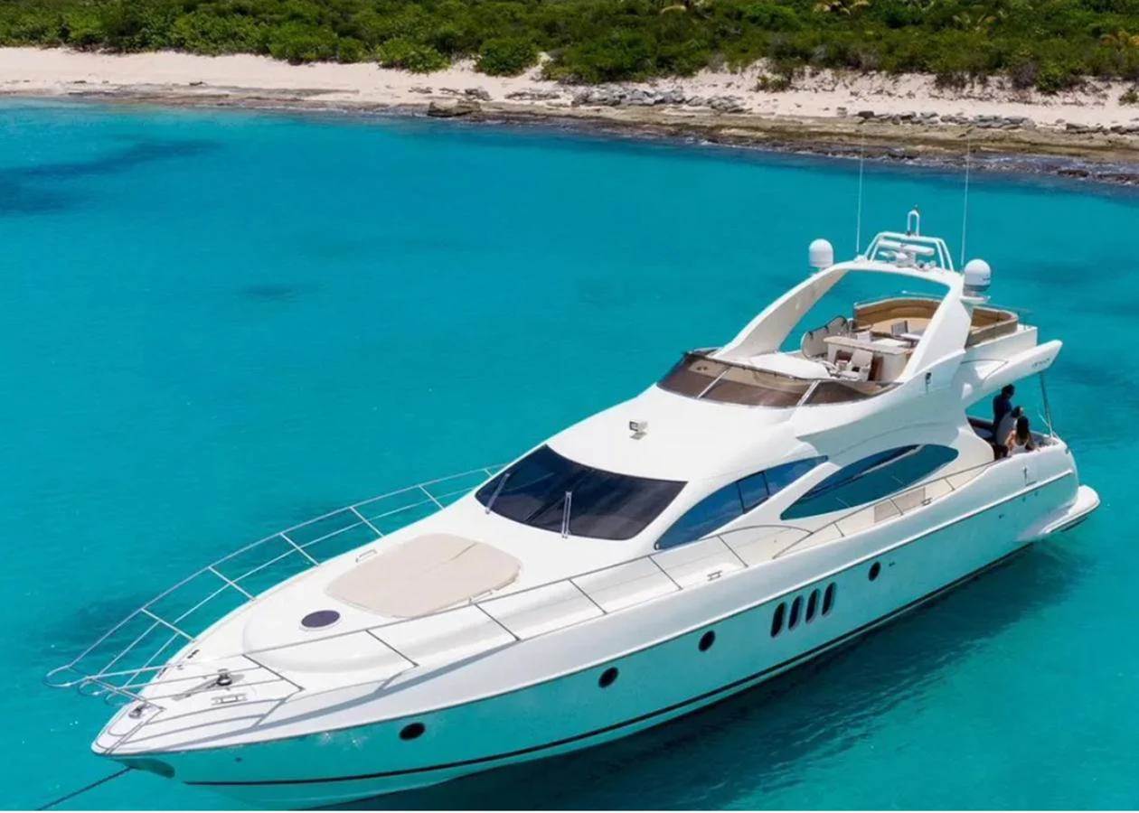 A sleek, modern yacht cruising in crystal-clear turquoise waters near a lush shoreline. aboard 2005 AZIMUT 68E Yacht for Sale