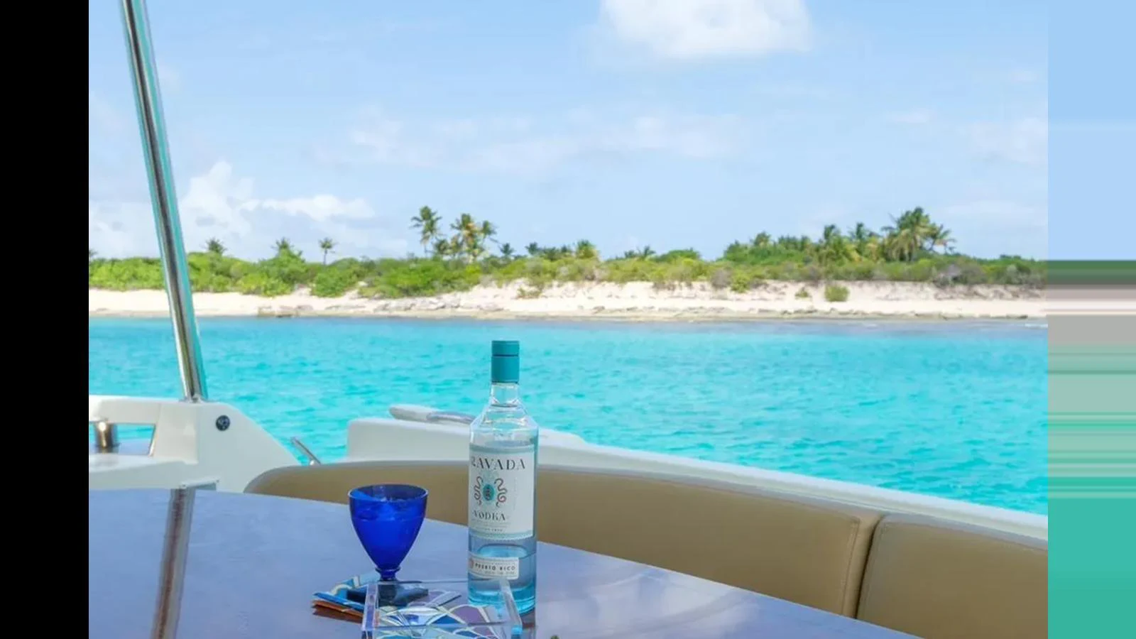 A serene view from the yacht's deck featuring a bottle of vodka and a blue glass against a backdrop of turquoise waters and a lush island. aboard 2005 AZIMUT 68E Yacht for Sale