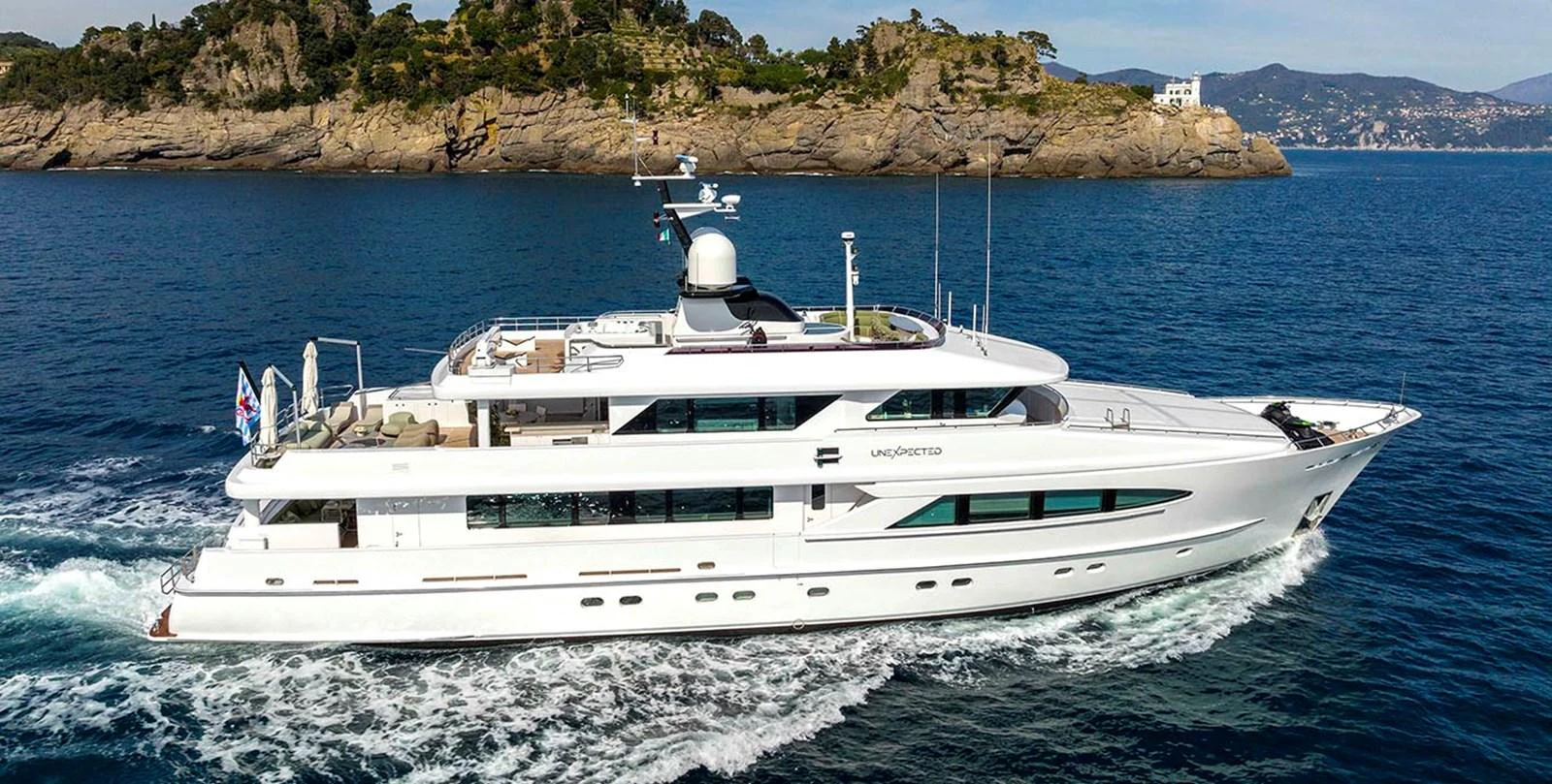 A sleek, modern yacht cruising along a picturesque coastline. aboard UNEXPECTED Yacht for Sale