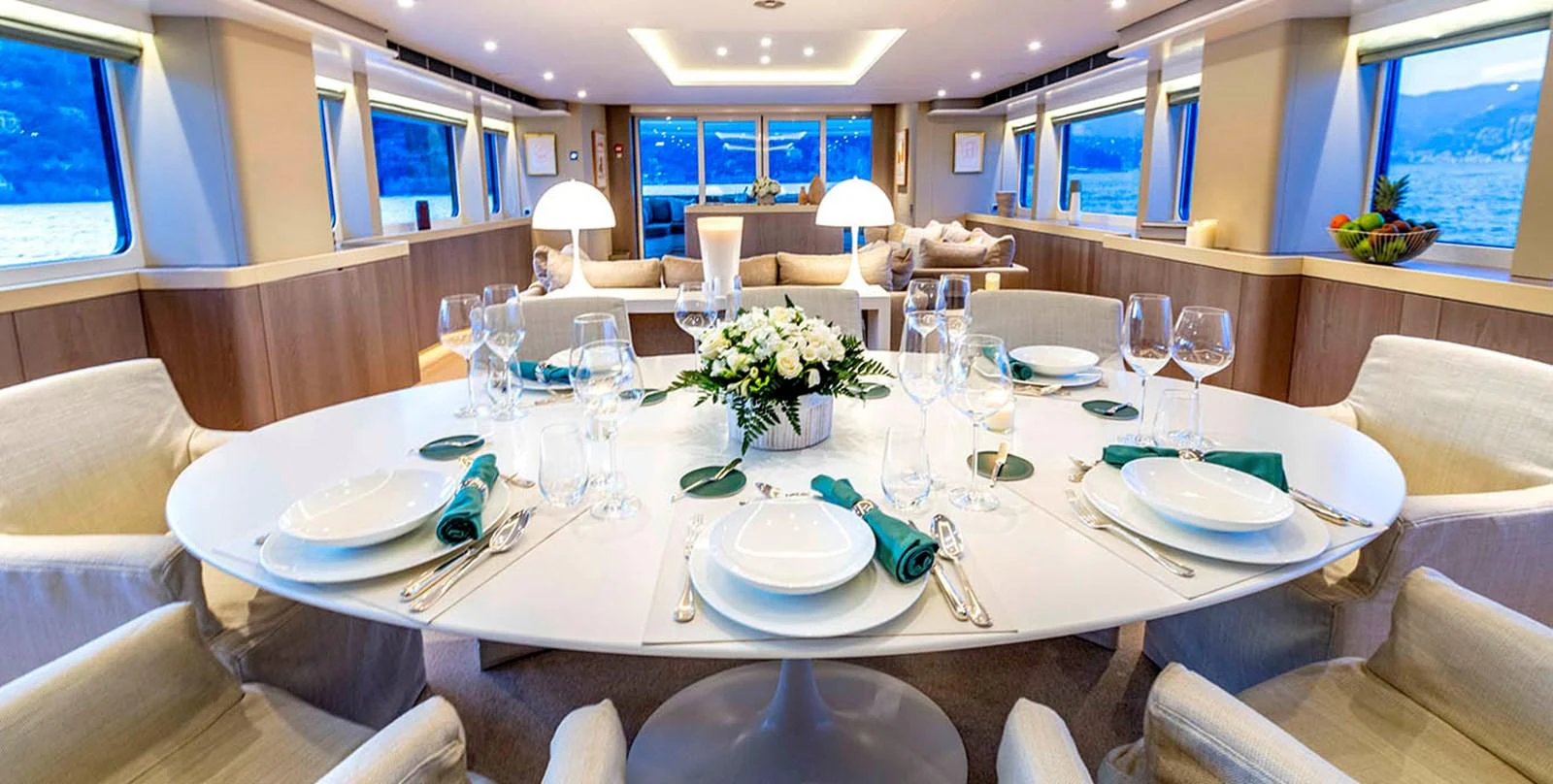 The yacht's dining area features an elegant table setting with panoramic views through large windows. aboard UNEXPECTED Yacht for Sale
