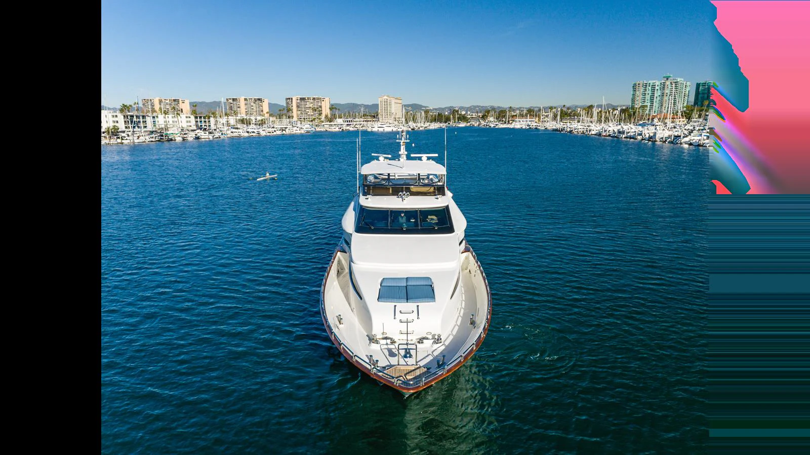 A luxurious yacht is seen head-on, cruising through a serene marina with a cityscape in the background. aboard ACTIVE OCTO Yacht for Sale