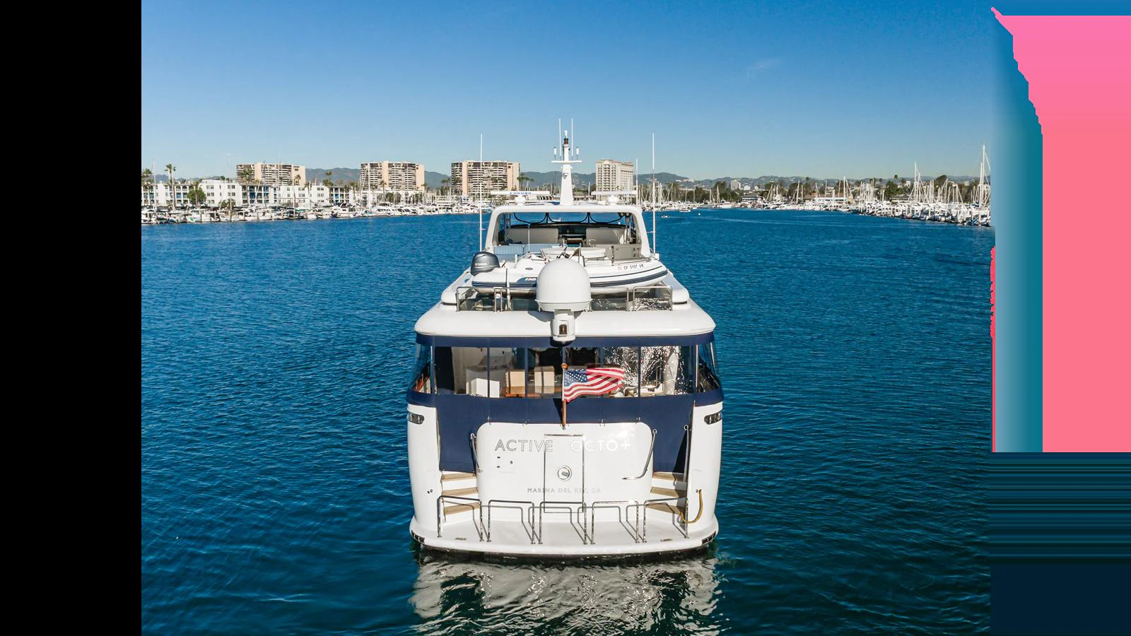 The yacht is seen from the rear, cruising in a serene marina with clear blue skies. aboard ACTIVE OCTO Yacht for Sale
