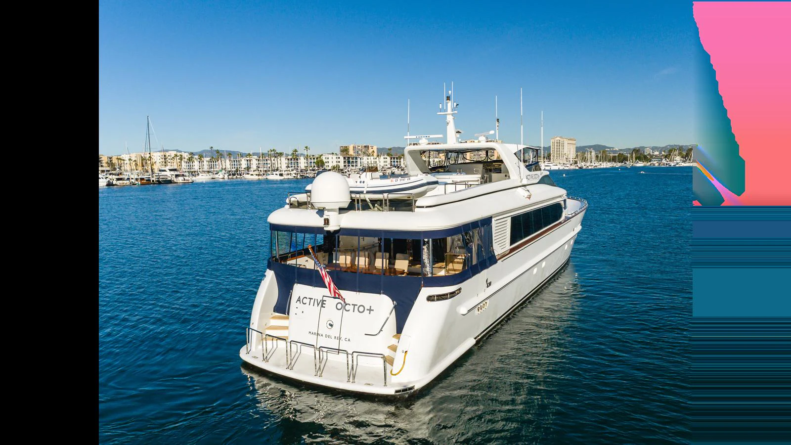 A sleek yacht glides through calm waters with a marina in the background. aboard ACTIVE OCTO Yacht for Sale