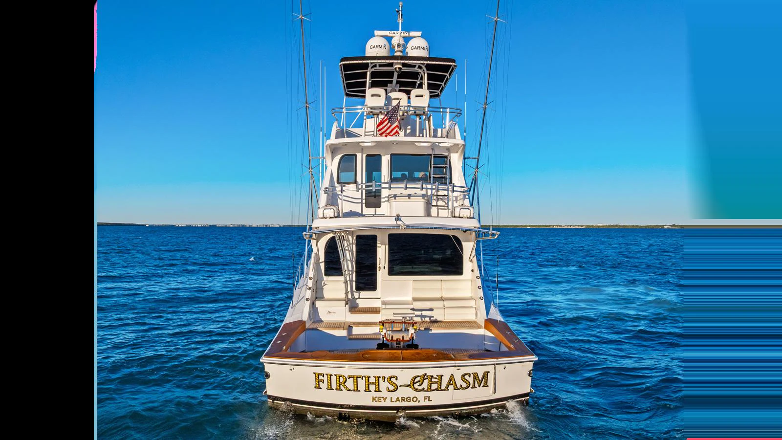 A luxurious yacht is seen from the rear, cruising on calm blue waters. aboard FIRTH'S CHASM Yacht for Sale