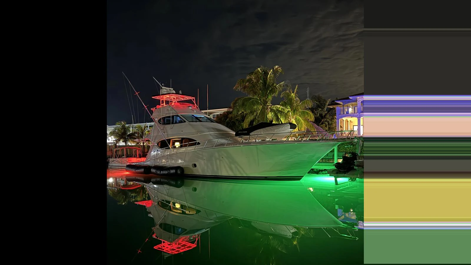A sleek yacht is docked at night, illuminated by vibrant green and red lights, reflecting beautifully on the calm water. aboard FIRTH'S CHASM Yacht for Sale