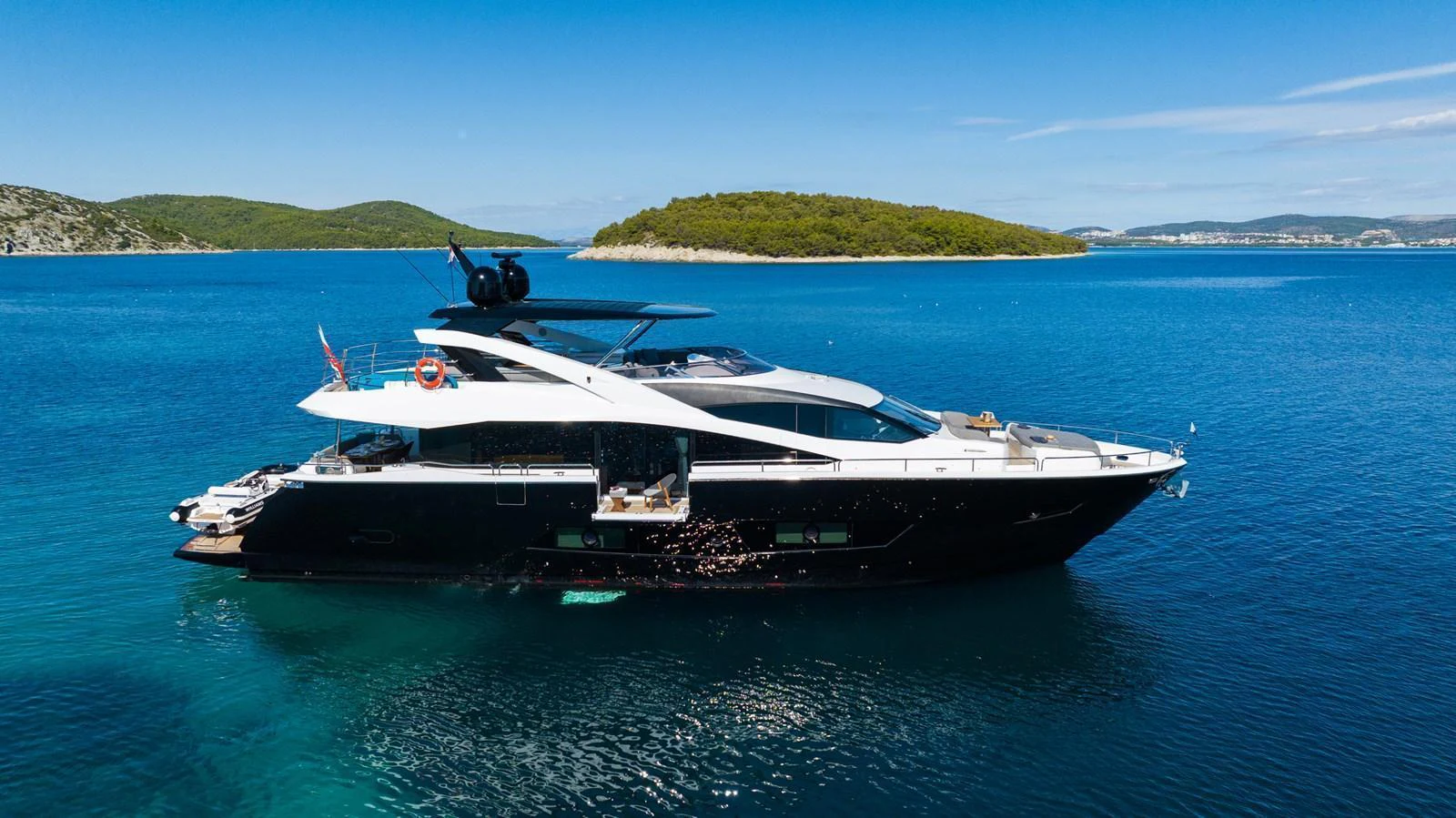 A sleek and modern yacht cruising on calm, clear waters with a scenic island in the background. aboard BLACK MAMBA Yacht for Sale
