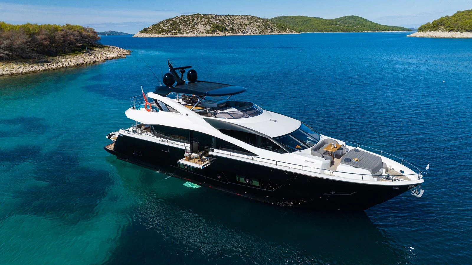 A sleek and modern yacht cruising in a serene, turquoise bay surrounded by lush, green islands. aboard BLACK MAMBA Yacht for Sale