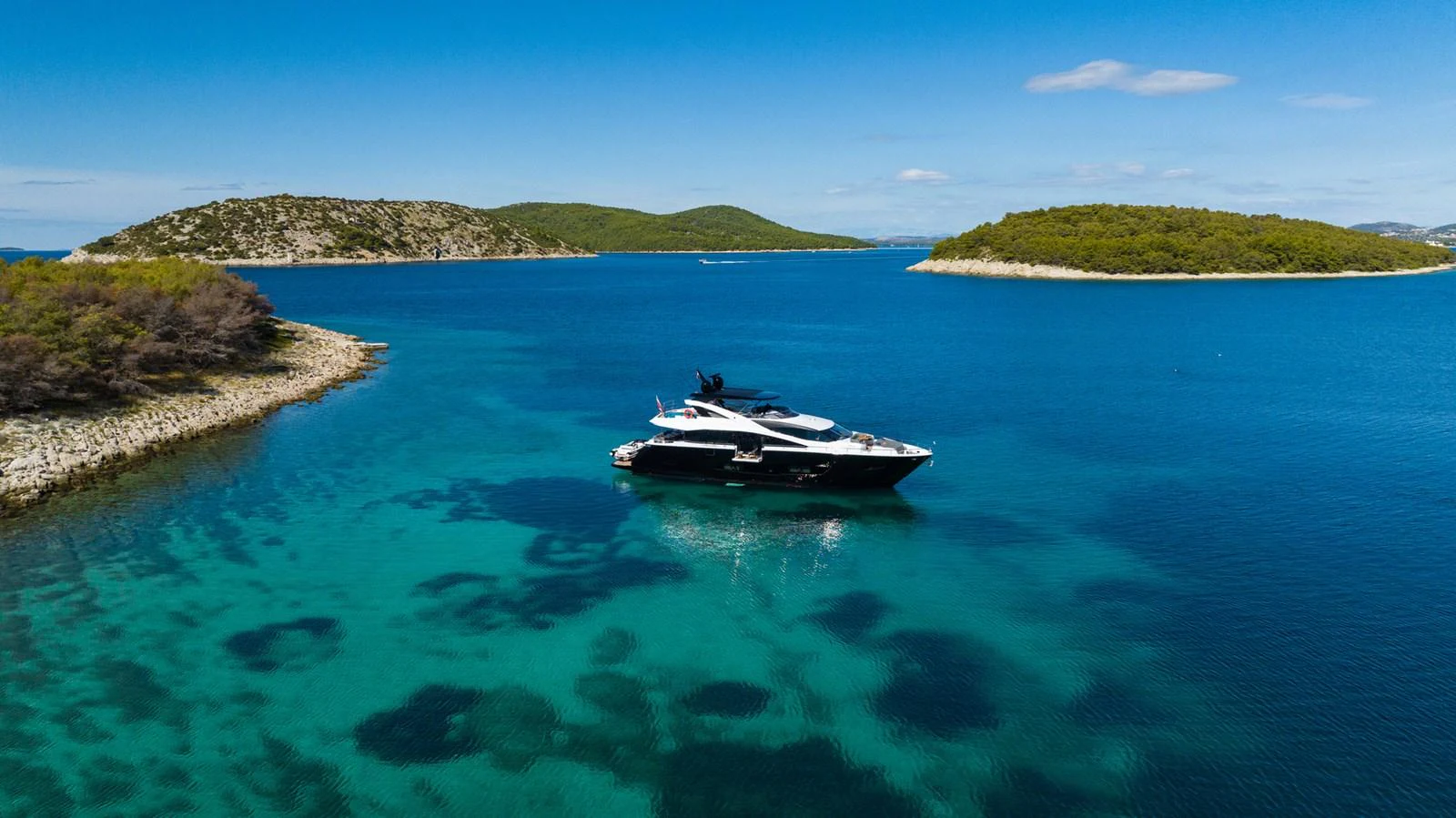 A sleek yacht cruises through crystal-clear turquoise waters surrounded by lush islands. aboard BLACK MAMBA Yacht for Sale