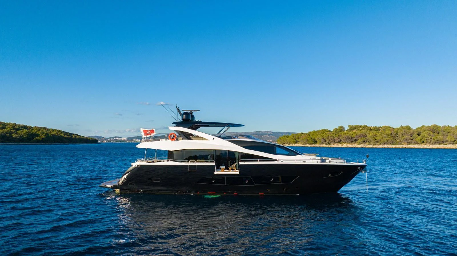 A sleek and modern yacht cruises through clear blue waters against a backdrop of lush greenery. aboard BLACK MAMBA Yacht for Sale