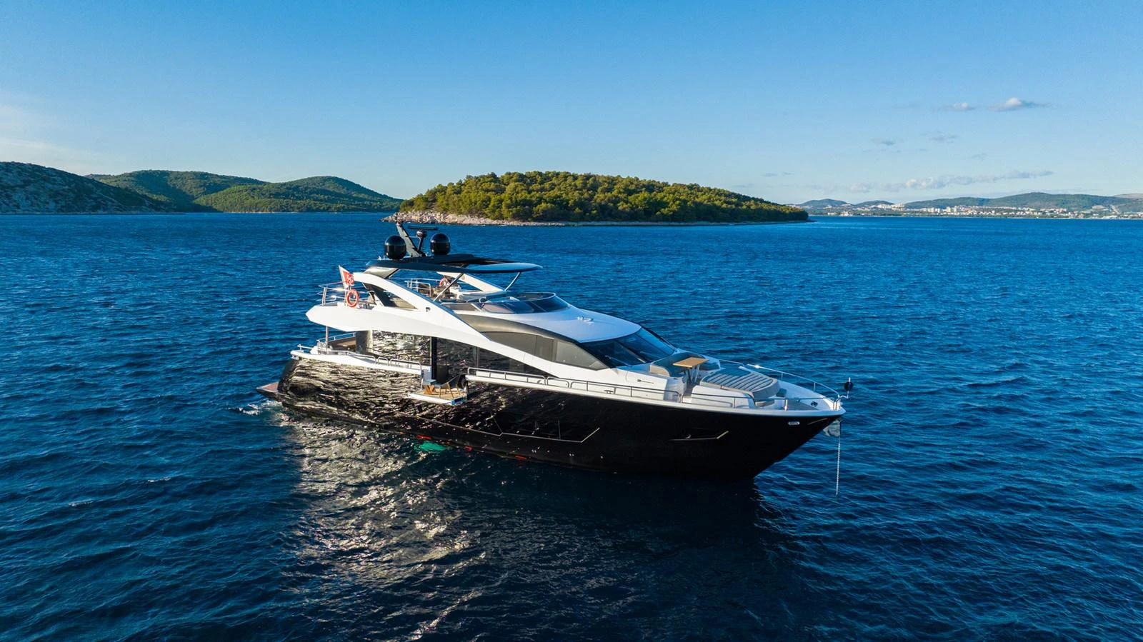 A sleek and modern yacht cruises through pristine blue waters with a scenic island backdrop. aboard BLACK MAMBA Yacht for Sale