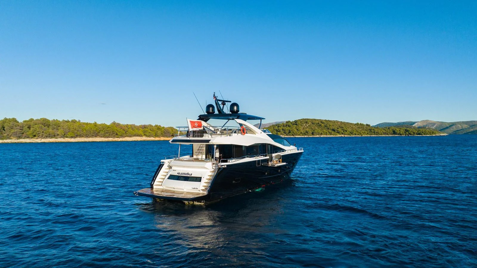 A sleek yacht cruises on calm blue waters with a scenic coastline in the background. aboard BLACK MAMBA Yacht for Sale