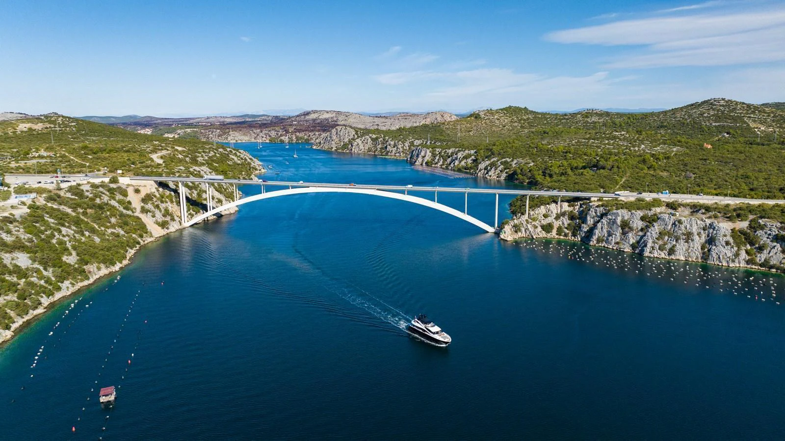 A yacht cruises through a serene waterway beneath a picturesque bridge, surrounded by lush landscapes. aboard BLACK MAMBA Yacht for Sale