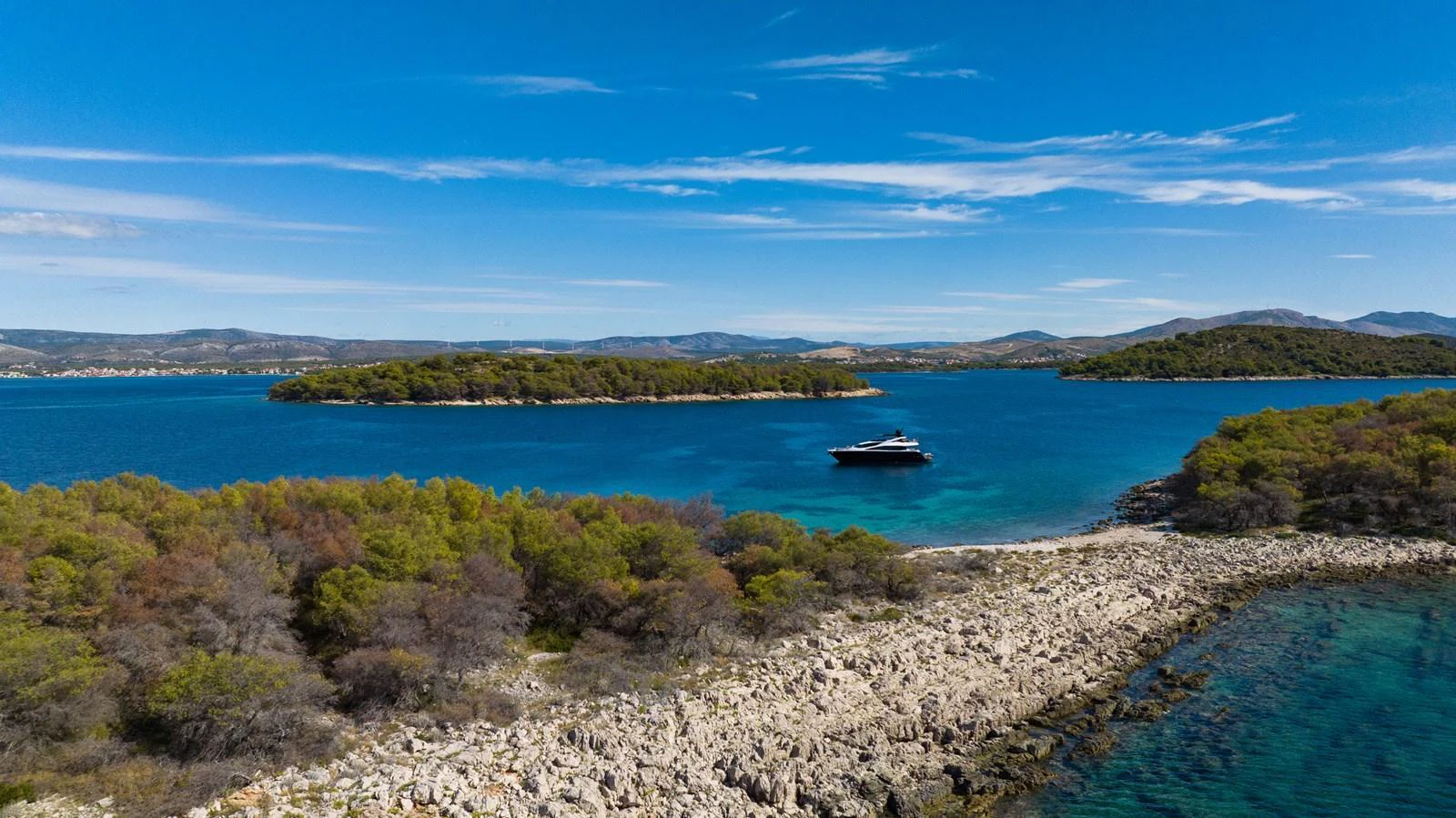 A sleek yacht cruises through a serene, turquoise bay surrounded by lush, rocky islands. aboard BLACK MAMBA Yacht for Sale
