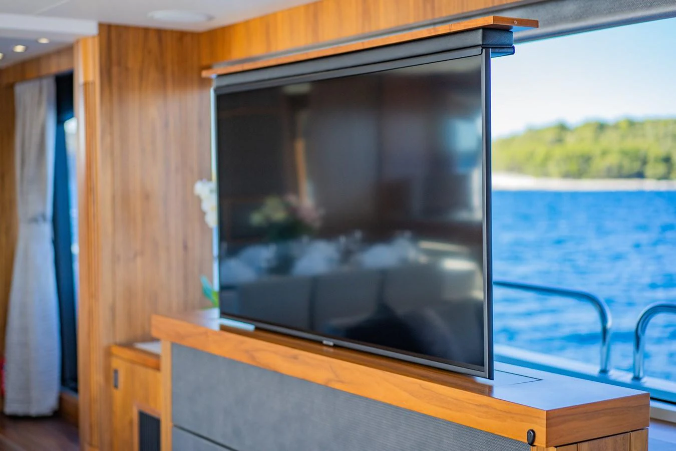 The yacht's interior features a sleek, modern entertainment area with a large flat-screen TV and wooden accents. aboard BLACK MAMBA Yacht for Sale