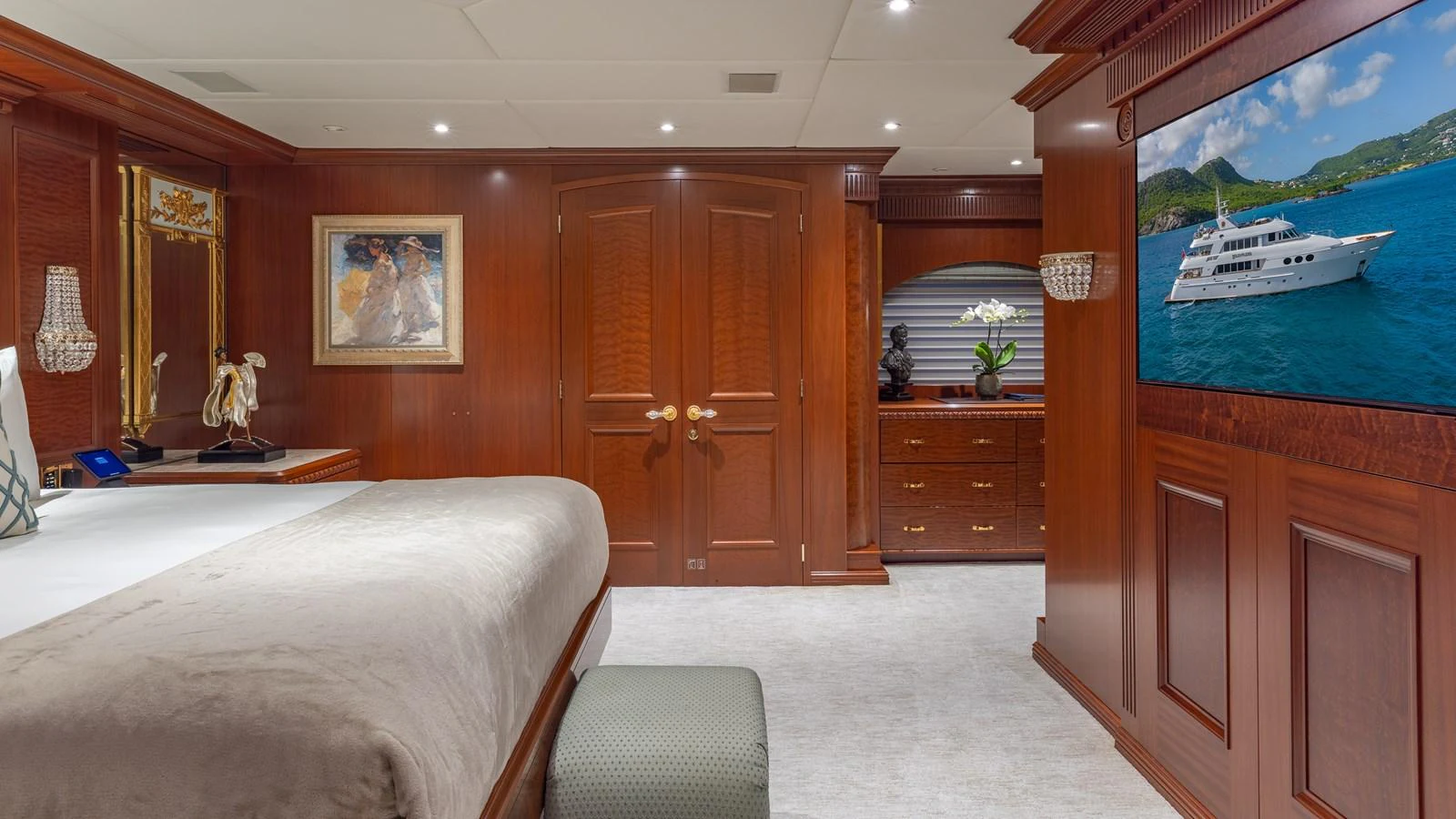 The stateroom features elegant wood paneling, a large bed, and a flat-screen TV displaying a yacht. aboard RELENTLESS Yacht for Sale