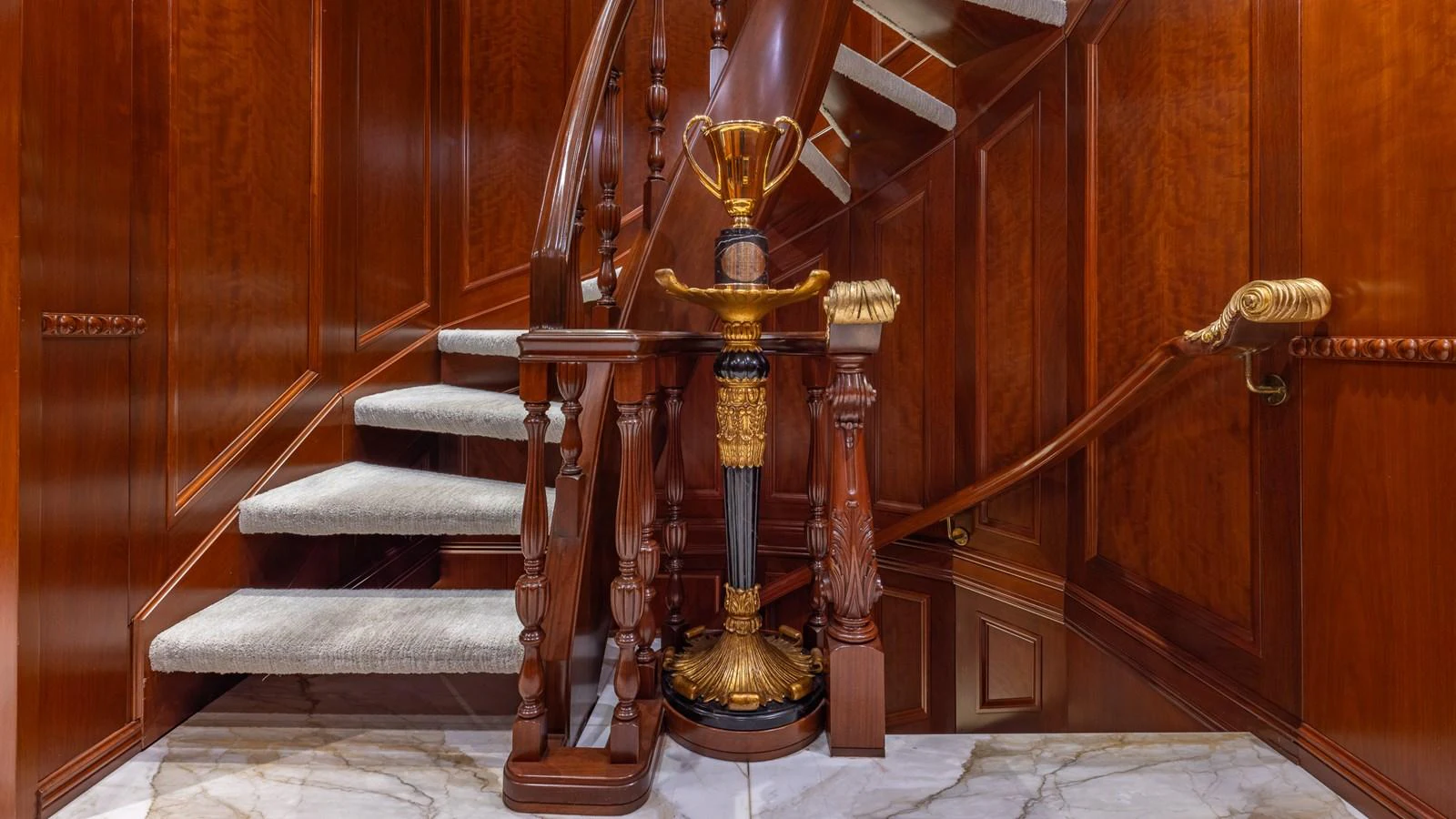 A luxurious wooden staircase with elegant detailing and a decorative trophy centerpiece. aboard RELENTLESS Yacht for Sale