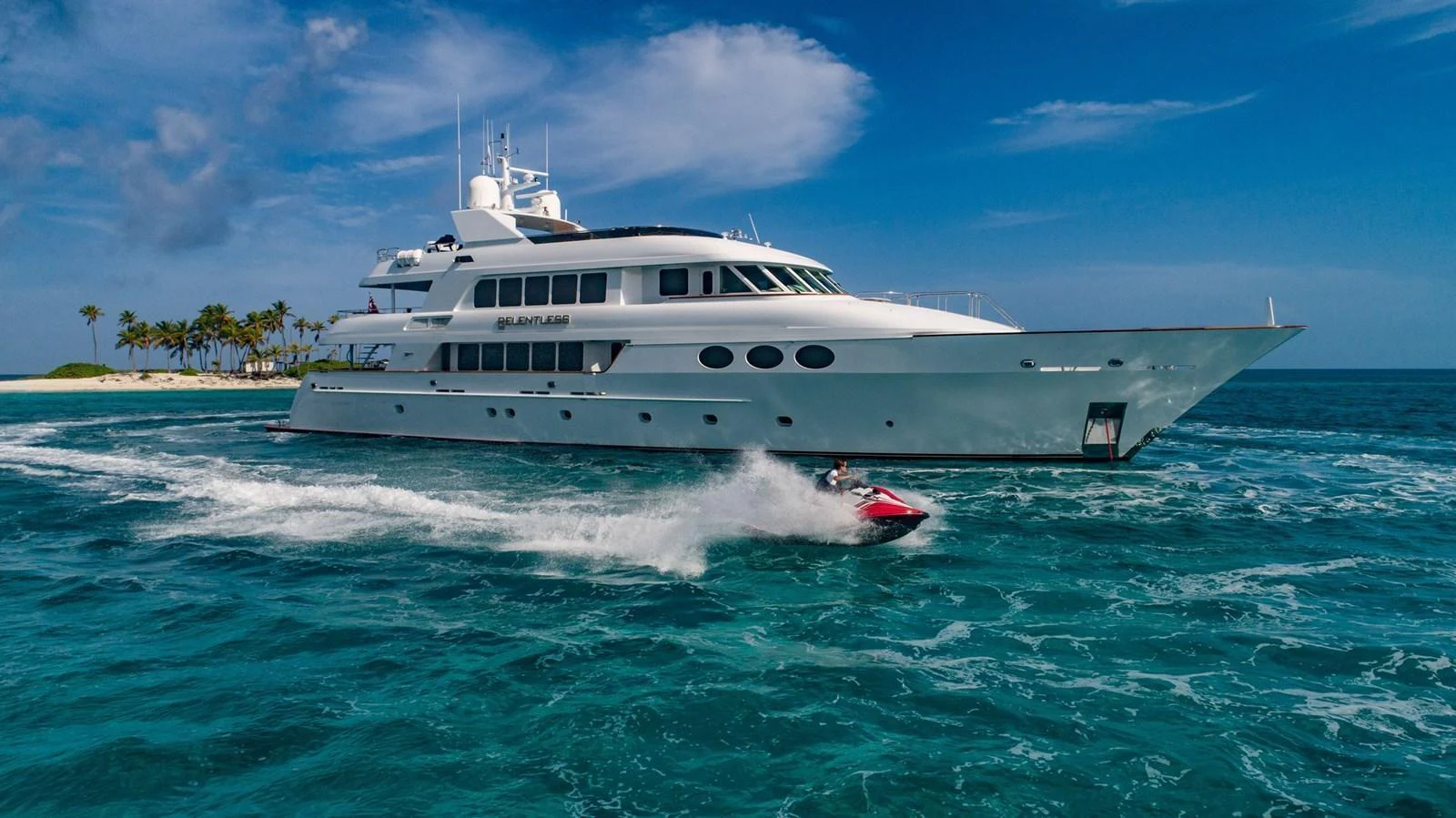 A sleek, white yacht cruises through clear blue waters under a bright sky. aboard RELENTLESS Yacht for Sale