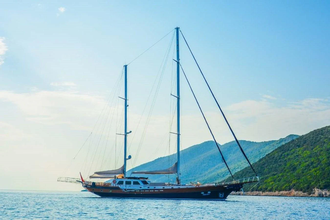 A stunning yacht sails gracefully on calm waters with a picturesque mountainous backdrop. aboard PAPA JOE Yacht for Sale