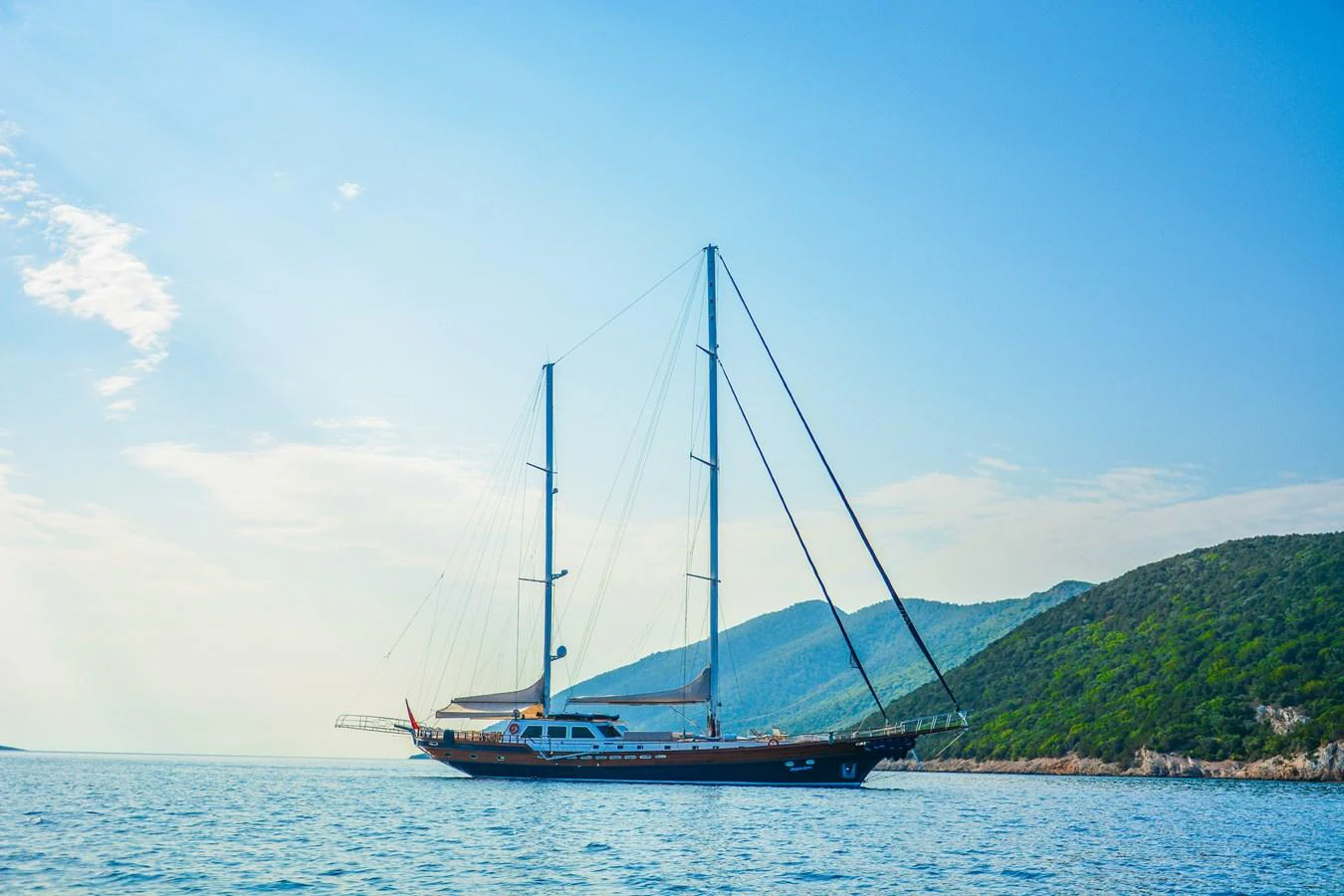 A stunning yacht sails gracefully on calm waters with a picturesque mountainous backdrop. aboard PAPA JOE Yacht for Sale