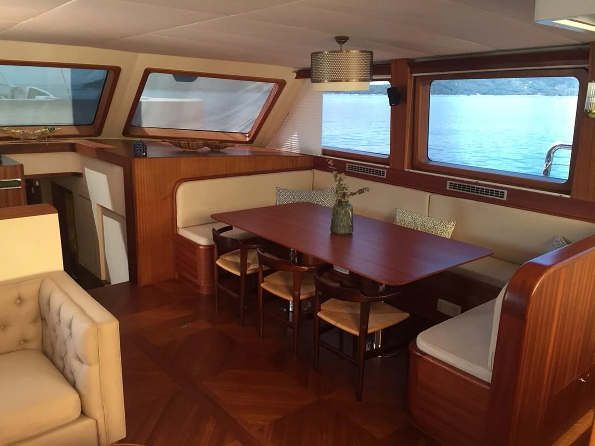 The yacht's dining area features a wooden table with seating for six, surrounded by large windows offering scenic views. aboard PAPA JOE Yacht for Sale