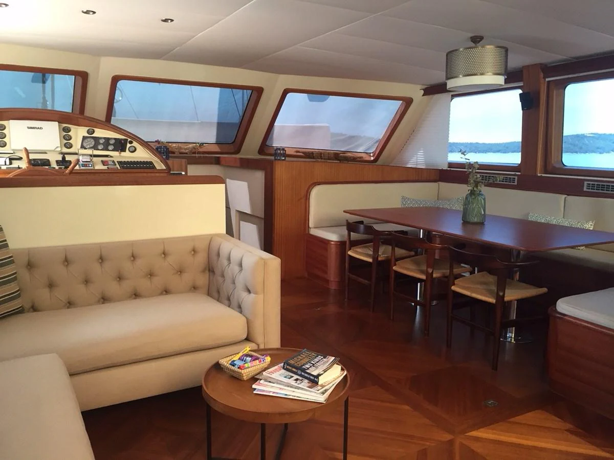 The saloon features a comfortable seating area with a dining table and panoramic windows offering scenic views. aboard PAPA JOE Yacht for Sale