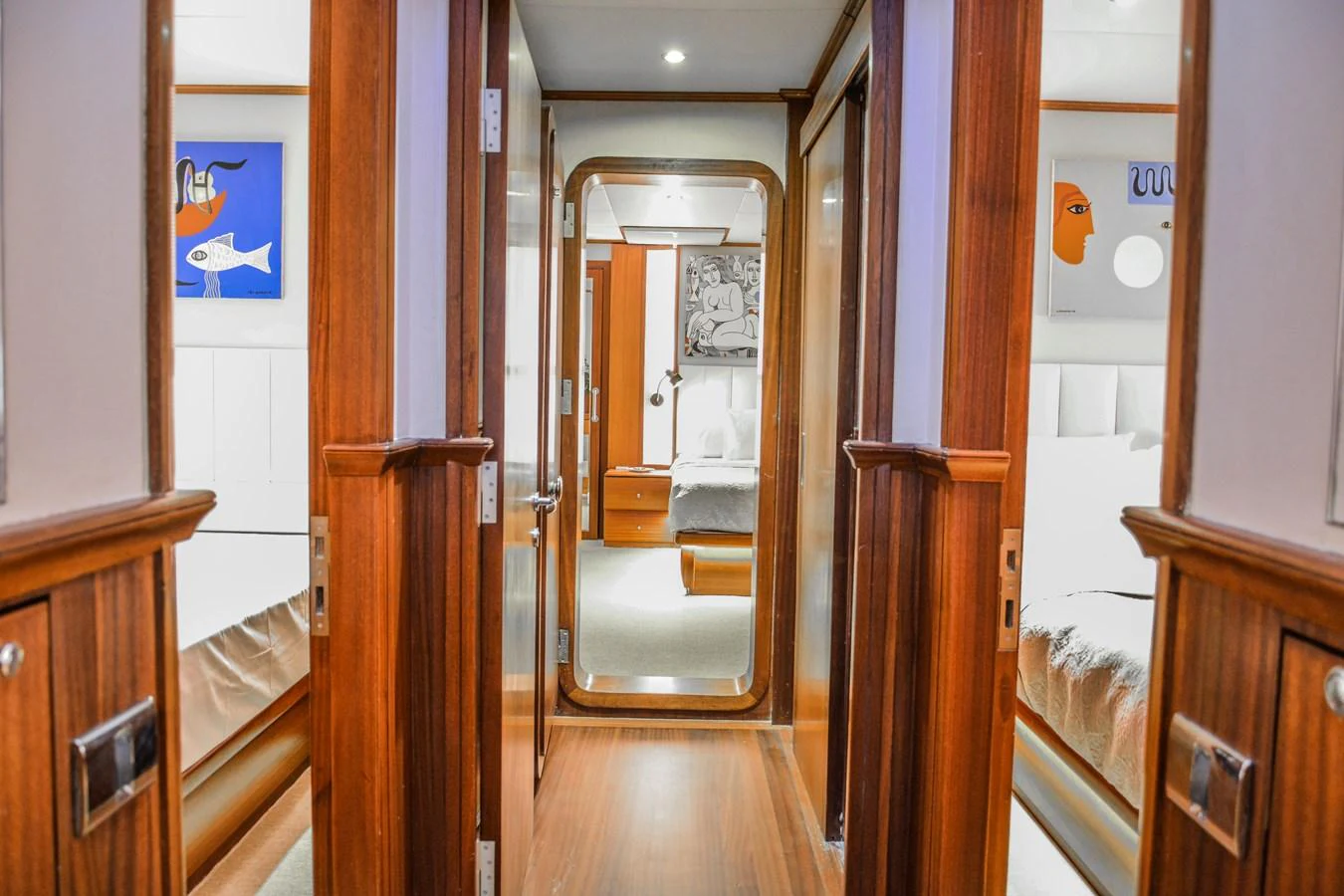 A luxurious hallway with wooden paneling and modern art leads to a cozy stateroom. aboard PAPA JOE Yacht for Sale