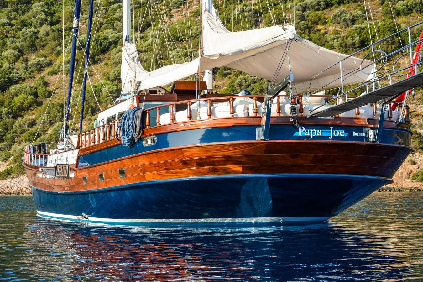 A classic wooden yacht with elegant lines is anchored in calm waters, showcasing its timeless design. aboard PAPA JOE Yacht for Sale
