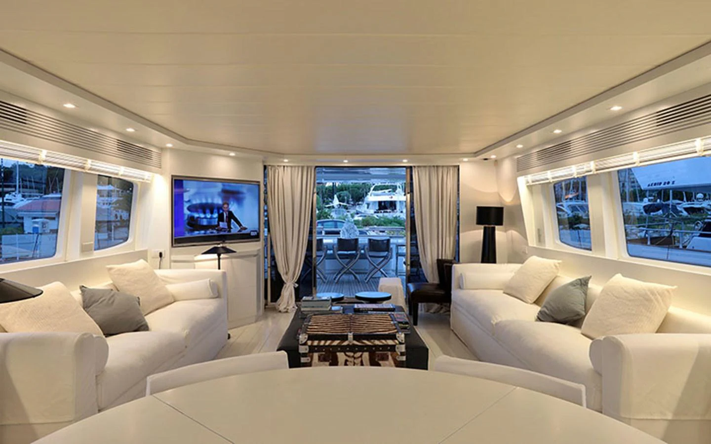 The spacious salon features elegant seating and a large flat-screen TV, opening to an aft deck with a dining area. aboard NIKCA Yacht for Sale
