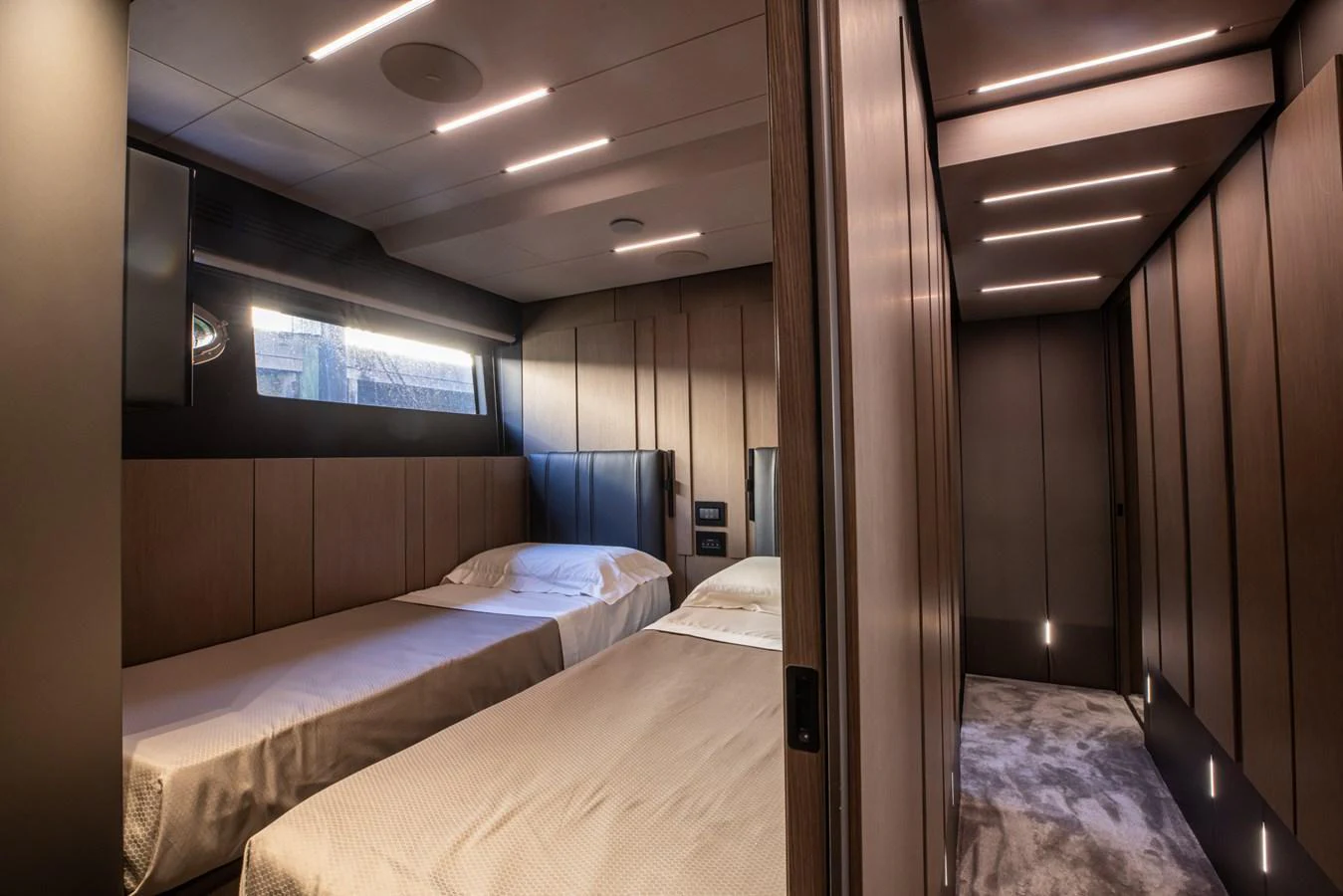 The guest stateroom features twin beds with modern lighting and sleek wood paneling. aboard CIAO Yacht for Sale
