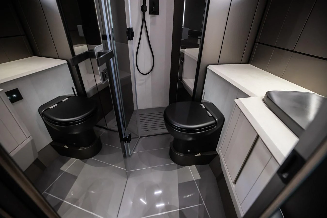 A sleek and modern yacht bathroom featuring dual black toilets and a minimalist shower area. aboard CIAO Yacht for Sale