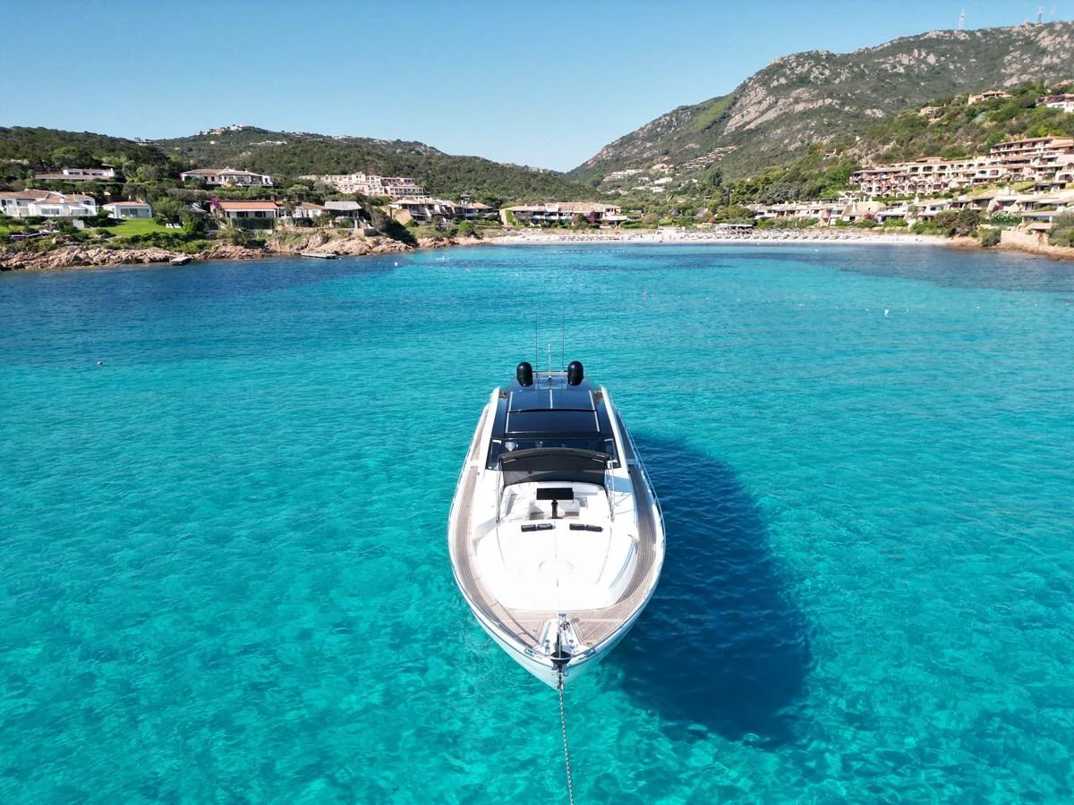 A sleek yacht is anchored in crystal-clear turquoise waters with a scenic coastal backdrop. aboard THYKE III Yacht for Sale