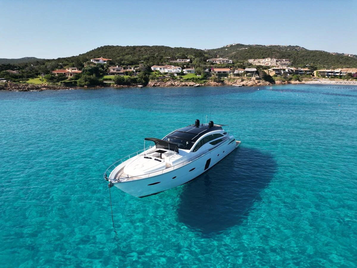 A sleek yacht is anchored in crystal-clear turquoise waters with a scenic coastal backdrop. aboard THYKE III Yacht for Sale