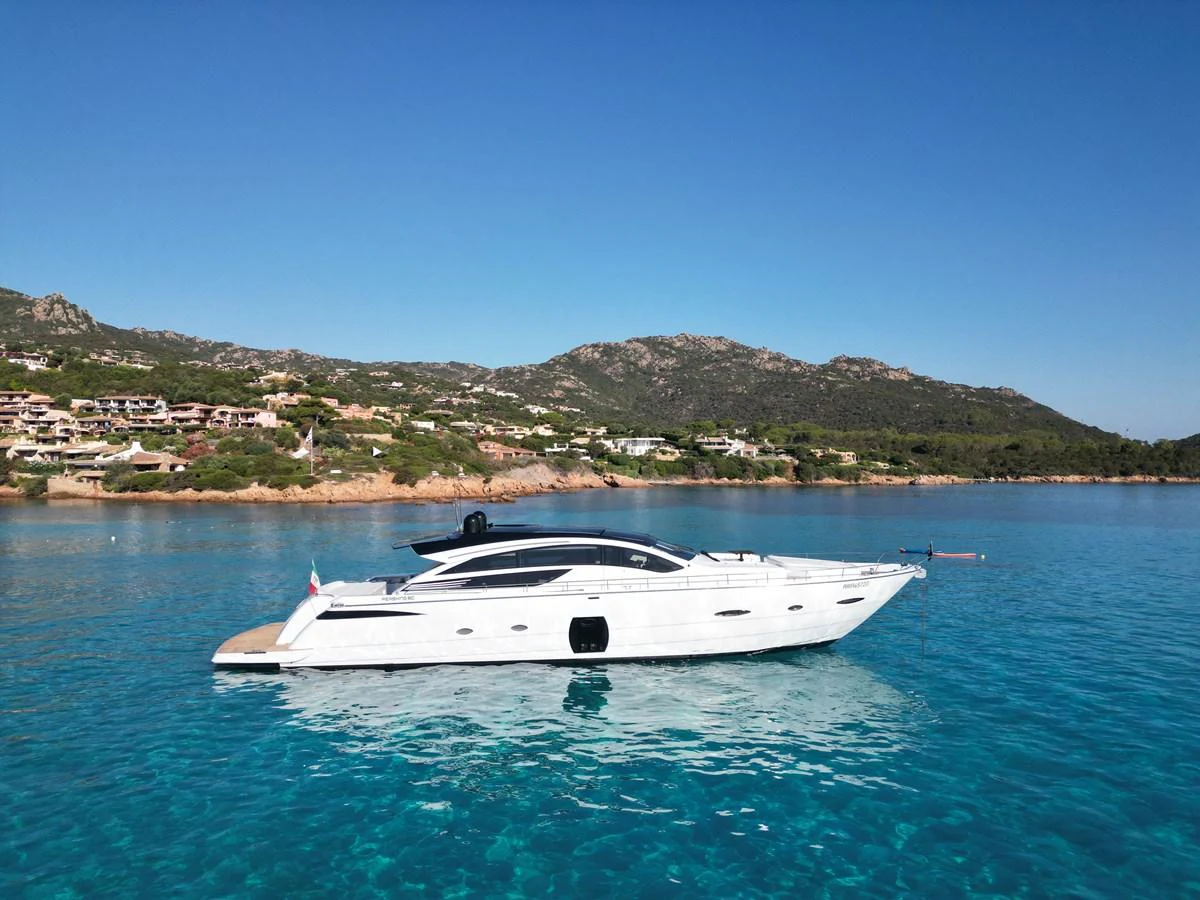 A sleek white yacht glides gracefully on clear blue waters with a scenic coastal backdrop. aboard THYKE III Yacht for Sale