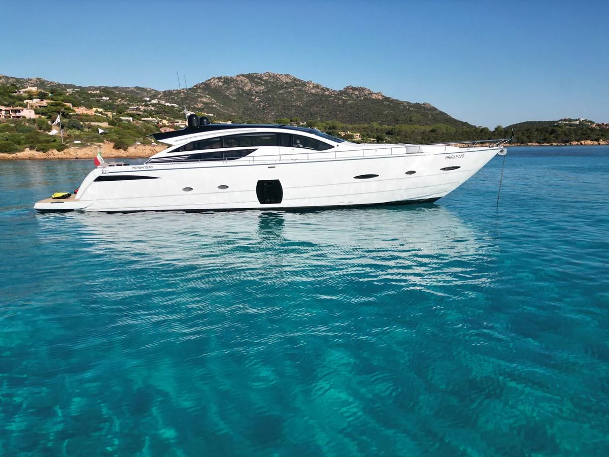 A sleek, modern yacht is anchored in crystal-clear turquoise waters with a scenic coastal backdrop. aboard THYKE III Yacht for Sale