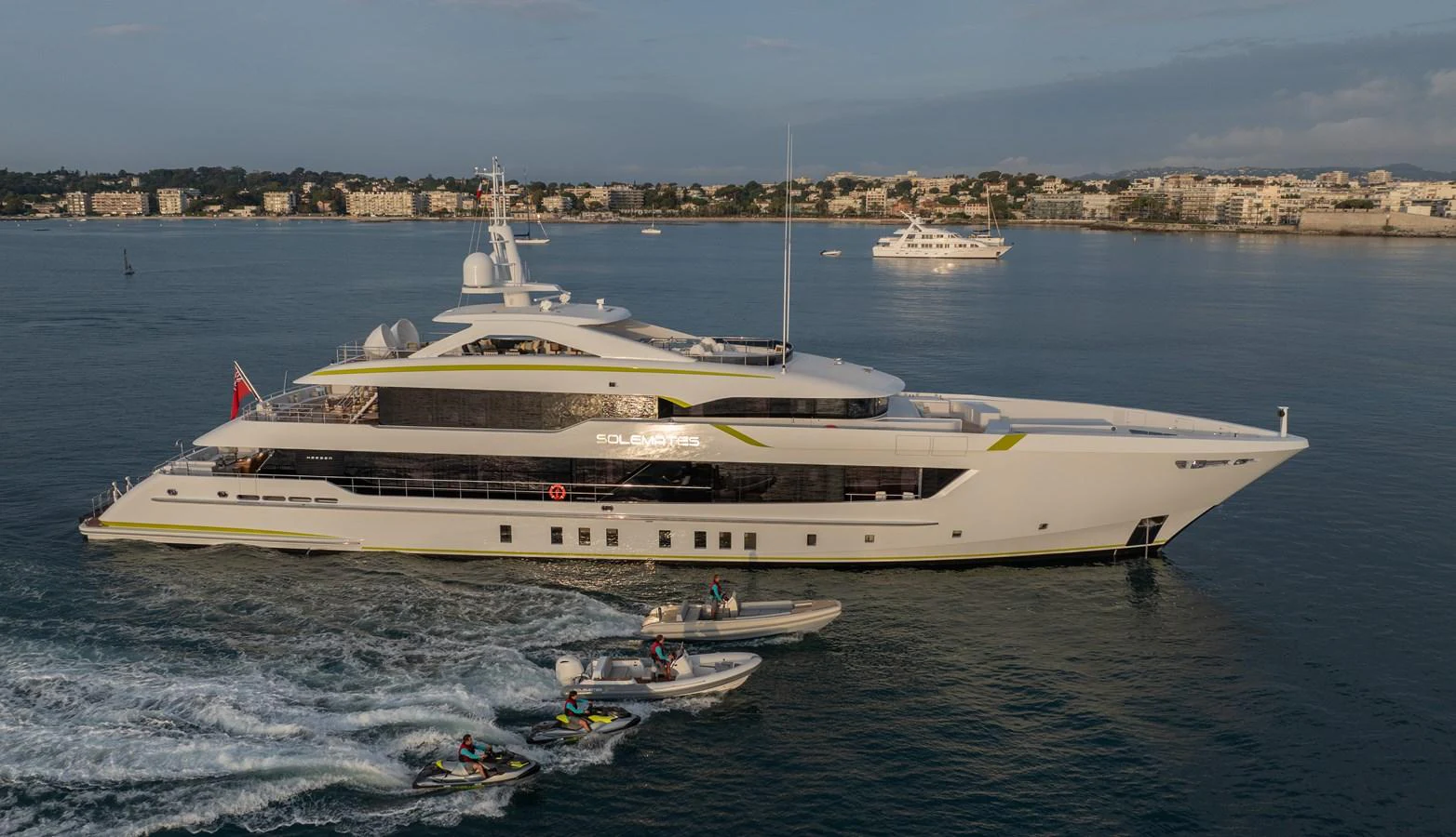A sleek and modern yacht cruises gracefully on calm waters, accompanied by several tenders and jet skis. aboard SOLEMATES Yacht for Sale