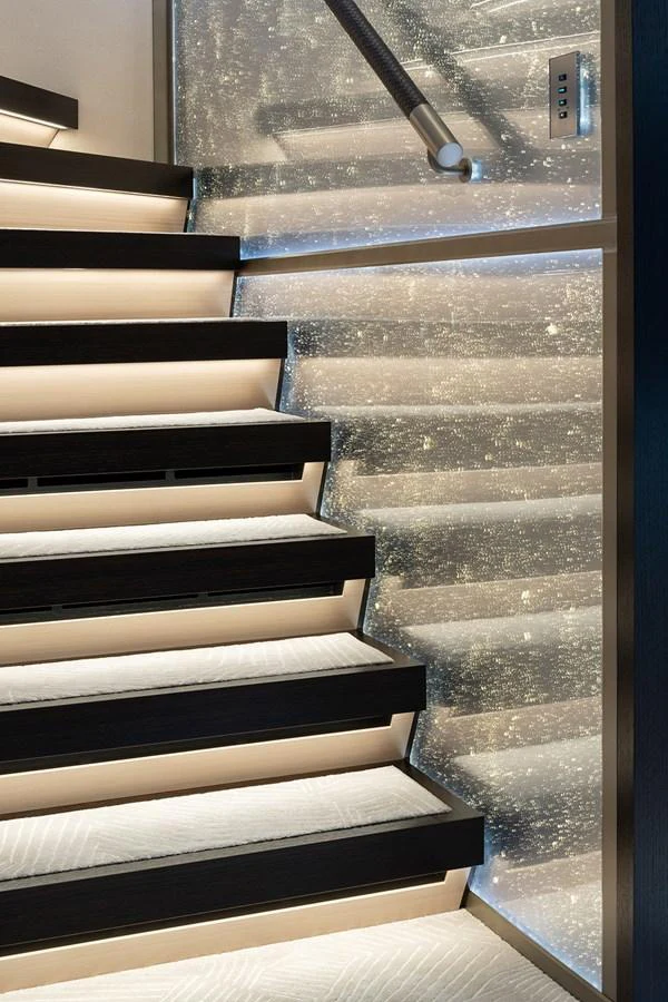 A modern staircase with sleek black steps and illuminated risers, complemented by a shimmering wall panel. aboard SOLEMATES Yacht for Sale