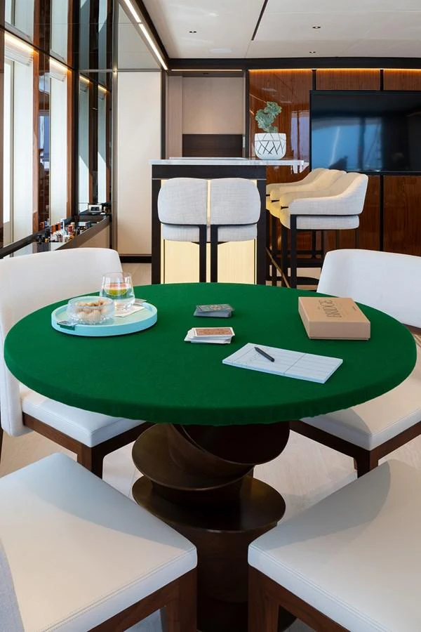 A cozy game room featuring a round table with cards and snacks, complemented by a bar area in the background. aboard SOLEMATES Yacht for Sale