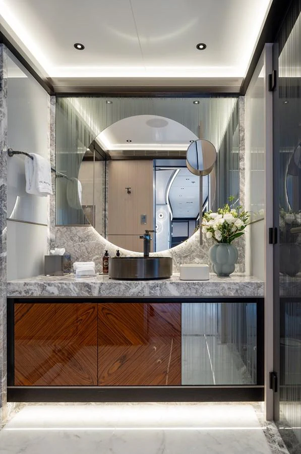 A luxurious yacht bathroom featuring a modern vanity with a round mirror and elegant marble accents. aboard SOLEMATES Yacht for Sale
