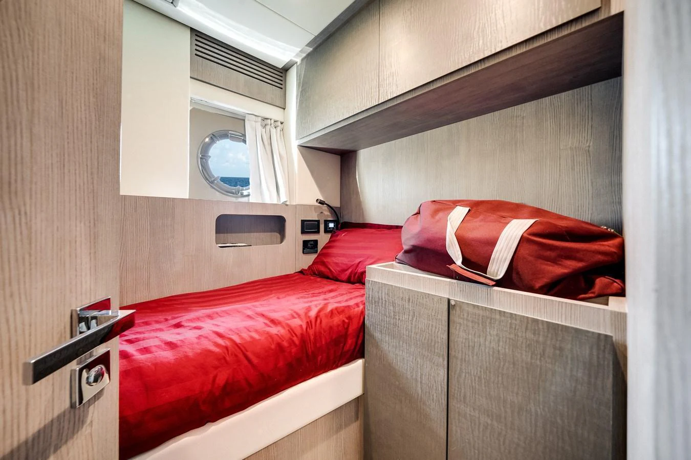 A cozy guest cabin with a single bed adorned with red bedding and ample storage space. aboard PARTNERSHIP V Yacht for Sale